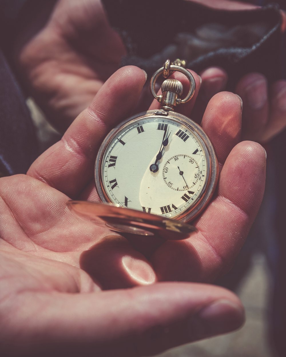 An open pocket watch with an enamel dial, held in two hands